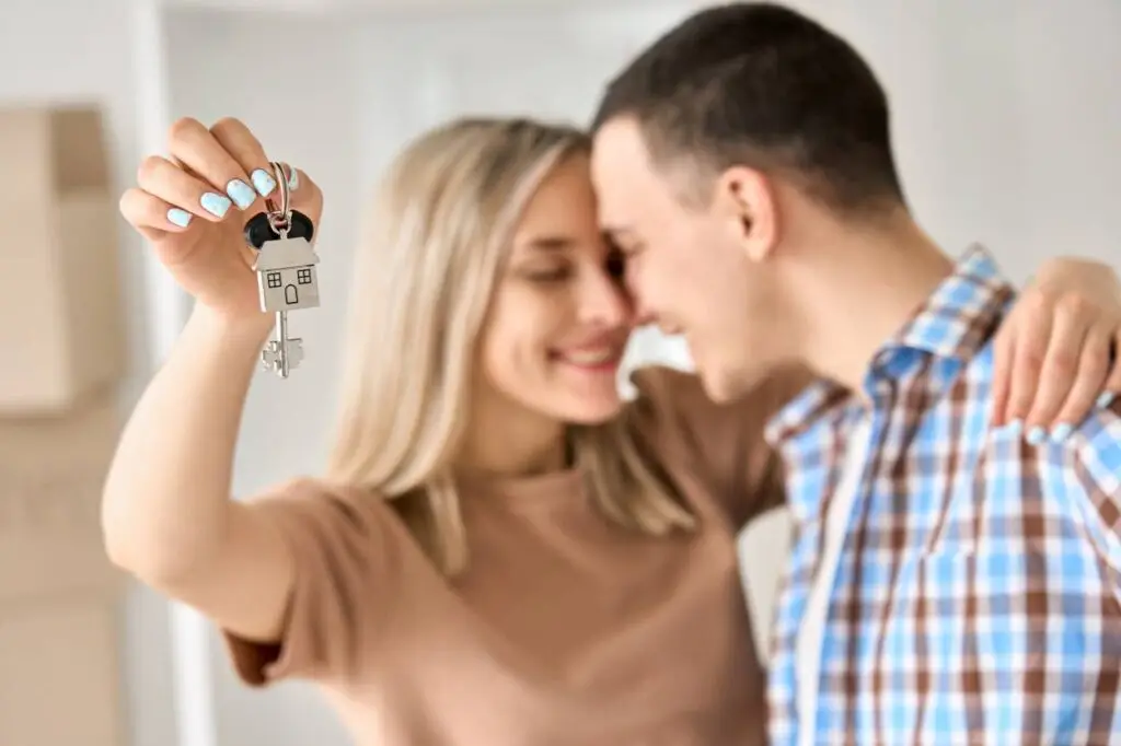 man and woman hugging holding up house key with house keyring